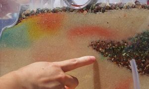 Colorful layers of sand and gravel as viewed through the wall of a small glass demonstration tank. Colorful dye highlights the path of water flow.